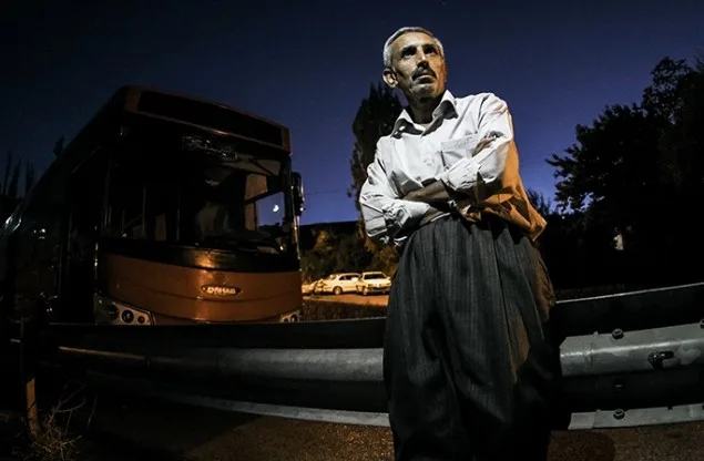 A man in a white shirt standing by a bus at night